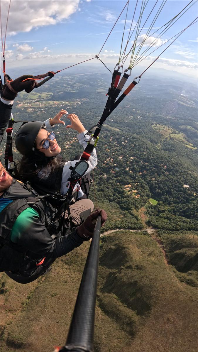 Voo duplo de parapente com passageira fazendo coração com as mãos