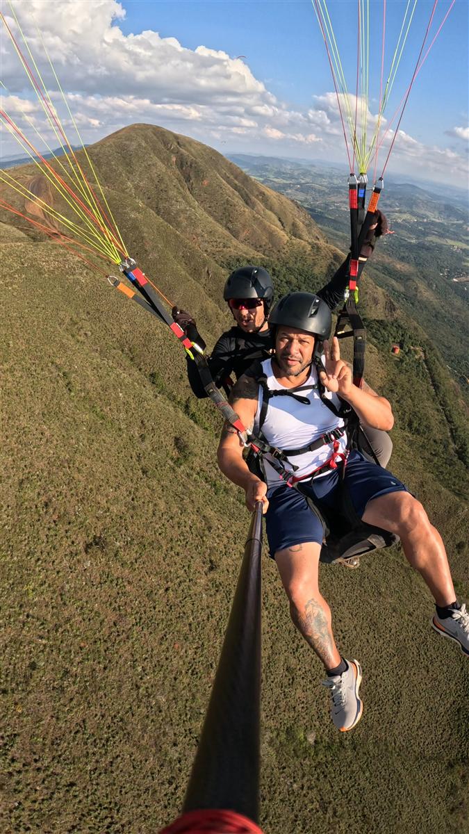 Voo duplo de parapente com passageiro fazendo sinal de paz na Serra da Moeda